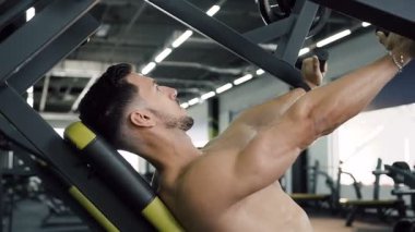 Genç adam spor salonunda spor egzersiz makineleri kullanarak silah kas pompalama spor.