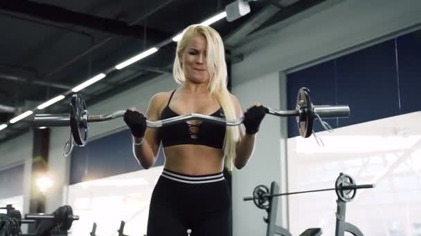 Chica trabajadora bombeando bíceps usando barras durante el entrenamiento en el gimnasio . — Vídeos de Stock