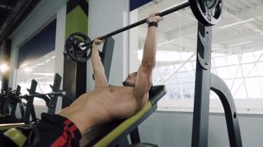 Yakışıklı çocuk silah Barbell bench basın spor salonu zemin üzerinde yukarı ve aşağı kas yükselterek pompalama.