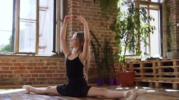 Een jonge slanke ballerina in een zwarte tutu maken bindgaren in de dansende hall. Mooie balletdanser beoefenen splitst pose meditatie genieten van gezonde spirituele lifestyle opleiding mindfulness oefening in — Stockvideo