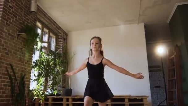 Привлекательная девушка-подросток, одетая в черное тело и юбку, практикующая балет в Студии. Грациозная балерина в черной пачке исполняет элементы классического балетного прыжка — стоковое видео