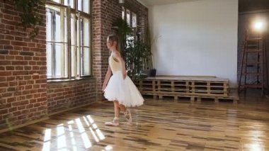 Genç balerin bir klasik bale pointe Ayakkabı ve tutu büyük pencere ve kırmızı tuğla duvar arka plan üzerinde gerçekleştirir. Zarif balerin dans pointe Ayakkabı ve elbise çırpınan bir beyaz