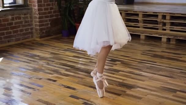 Young ballet dancer in white ballet shoes and skirt practices ballet dance on the wood floor. Young ballerina in white pointe shoes dances on tiptoe at ballet school — Stock Video