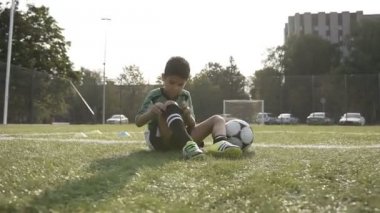 Küçük çocuk futbol sahasında futbol tozluk sabitleme zor eğitimden sonra siting.