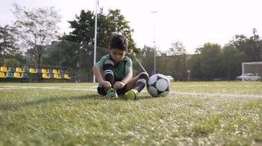 Küçük çocuk futbol sahasında sert futbol sahası sonra istirahat ederken ayakkabılarına sabitleme.