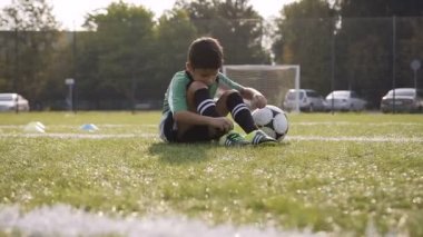 Futbol sahasında siting ayakkabılarına sabitleme küçük futbolcu.