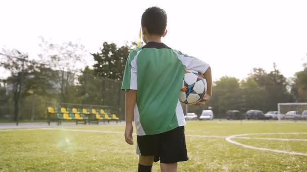 Niño pequeño caminando con pelota de fútbol en la mano . — Vídeo de stock