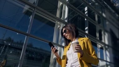 Takım elbise içinde büyük modern ofis merkeze yakın yürüme beyaz emin başarılı işkadını smartphone kullanır ve güneşli günde kahve içiyor. Açık