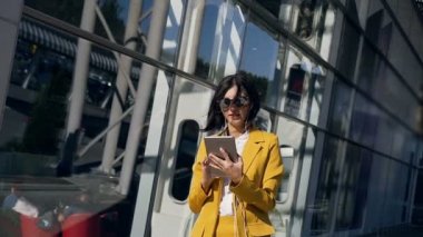 Takım elbiseli Genç iş kadını bir öğle yemeği molası sırasında modern cam İş Merkezi yakınındaki tablet bilgisayarda çalışıyor. İş, teknoloji ve insan kavramı
