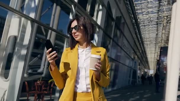 Крупный план молодой профессиональной предпринимательницы в классическом костюме использует смартфон и пьет кофе на городской улице во время рабочего обеденного перерыва — стоковое видео