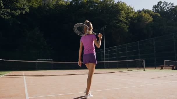 Achteraanzicht van de jonge vrouw in het uniform van de tennis wandelen op de rechtbank. — Stockvideo