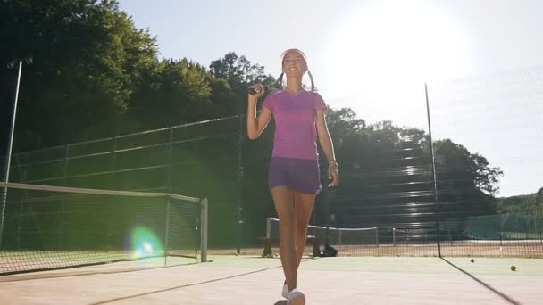 Söta leende flicka med tennisracket promenader på tennisbanan. — Stockvideo