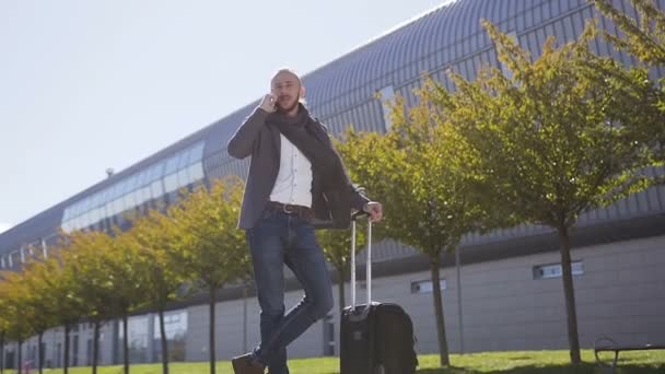 Homme cadre publicitaire caucasien avec valise parler sur le smartphone à l'extérieur près de l'immeuble de bureaux moderne. Concept de technologie, téléphonie, voyages d'affaires, business, wall street — Video