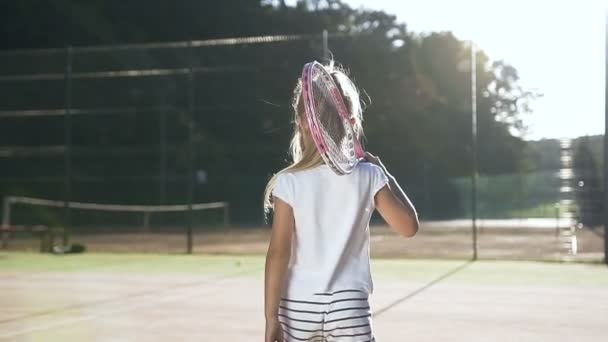 Liten flicka med tennisracket gå på domstolen. — Stockvideo