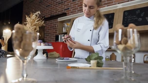 Unga kvinnliga kocken ansluta två halvor av mandelbiskvier med grädde. — Stockvideo