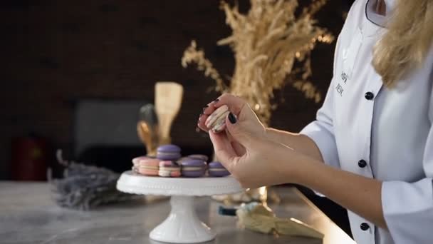 Plan rapproché des mains de la femme reliant deux moitiés de macarons à l'aide de crème. Inscription sur le tablier, nom du modèle Nina Leus — Video