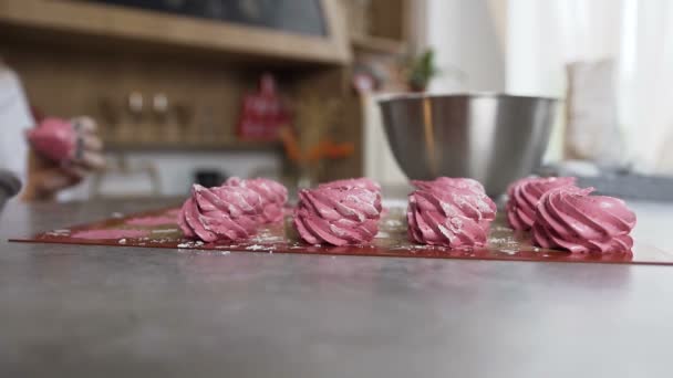 Mãos de mulher colocando marshmallows rosa na mesa na cozinha . — Vídeo de Stock