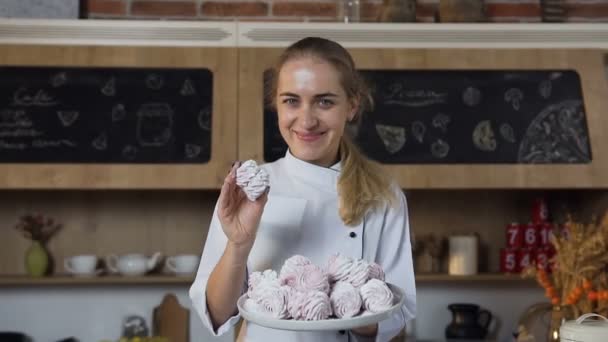 Όμορφα Γυναικεία baker χαμογελά στη φωτογραφική μηχανή με ένα πιάτο marshmallows. — Αρχείο Βίντεο