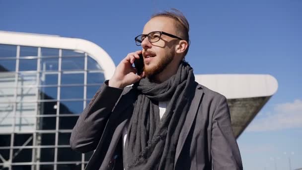Atractivo hombre de negocios en una hermosa chaqueta con bufanda hablando por teléfono, caminando cerca del edificio de oficinas, riendo y luciendo muy feliz — Vídeo de stock