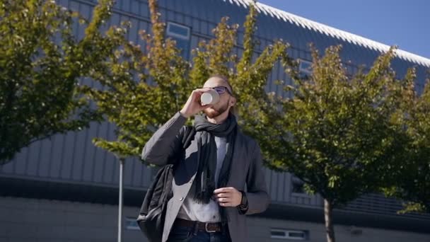 Retrato de un joven hombre de negocios serio en una chaqueta con bufanda caminando por la ciudad, tomando café y mirando los relojes. Concepto de nuevo negocio, viaje de negocios, banquero, gerente — Vídeos de Stock