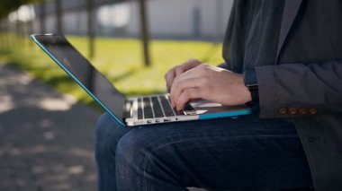 Yakın çekim. Erkek tipik bilgisayar klavye üzerinde eller. Açık havada. Tezgah ve uses laptop oturan genç iş adamı. Adamın parmakları dizüstü klavye üzerinde kelime yazarak