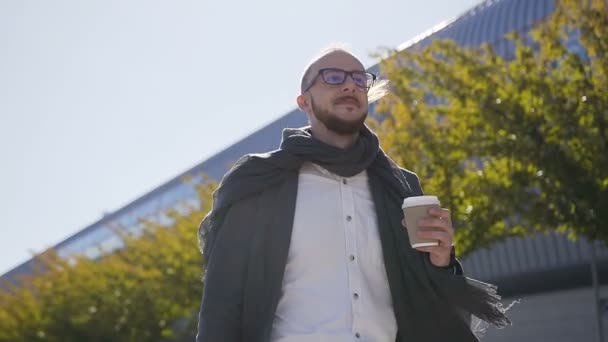 Retrato del guapo hombre de negocios caucásico en vasos caminando por la calle cerca del edificio de oficinas, tomando café y llevando una maleta. Al aire libre — Vídeo de stock