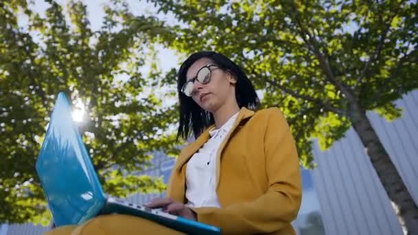 Retrato de mujer de negocios atractiva joven utiliza el ordenador portátil en un descanso al aire libre, hermosa estudiante sentada en el banco en el parque y escribiendo el texto en el ordenador portátil. Al aire libre — Vídeos de Stock