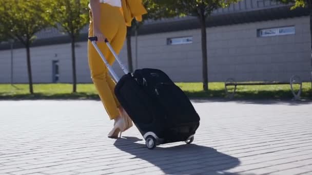 Λεπτή γυναίκα με κομψό κοστούμι τραβά μια βαλίτσα, σπεύδει να μια επαγγελματική συνάντηση. Ελκυστική γυναίκα πηγαίνει σε ένα επαγγελματικό ταξίδι, τραβώντας τη βαλίτσα της κατά μήκος του πεζοδρομίου πίσω της στα πόδια της — Αρχείο Βίντεο
