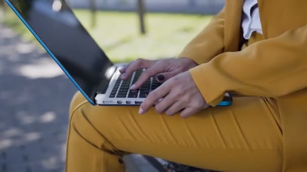 Close-up de uma mulher mãos digitando no teclado do computador. Ao ar livre. Jovem mulher de negócios de terno sentado no banco e mãos digitando em um teclado de computador, escrever artigo, escrever relatório — Vídeo de Stock