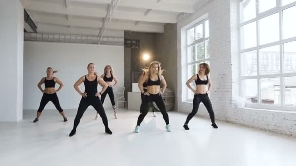 Fitness osztály csoport egy hat fiatal nők fekete sport ruhák végre fitness gyakorlatok. Fitness lányok végre ugrás fehér sport osztály a helyszínen — Stock videók