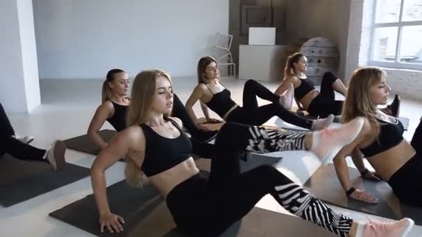 Grupo de jovens atletas mulheres com instrutor realiza ginástica aeróbica no chão em aula de fitness. Conceito de ioga, fitness, esporte, treinamento, aeróbica e estilo de vida saudável — Vídeo de Stock