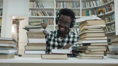 Mutlu Afrika erkek öğrenci kulaklık ve kütüphanede masada otururken dans müzik dinleme.