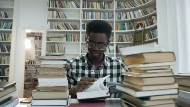 Portrét africké mladý muž v brýlích, čtení knihy při posezení v knihovně.