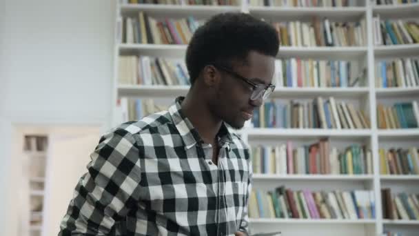 Dolly filmou um estudante africano caminhando pela biblioteca, dando cinco a uma estudante africana atraente e começando a estudar juntos na biblioteca. . — Vídeo de Stock