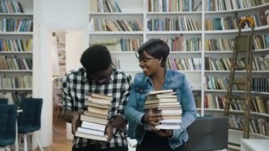 Kitap bir sürü sırasında sohbet ve Kütüphane arka plan üzerinde gülüyor elinde tutan genç Afrikalı çift.