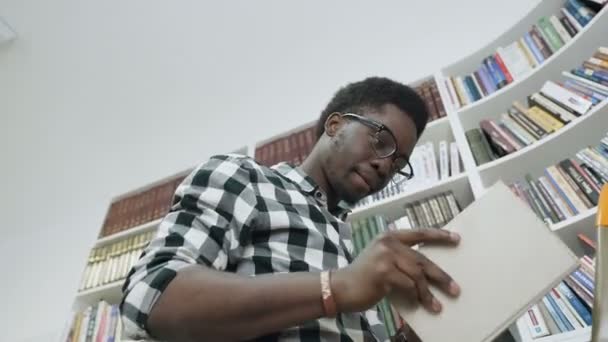 Africano livro de leitura do estudante do sexo masculino, enquanto em pé na escada na biblioteca da universidade . — Vídeo de Stock