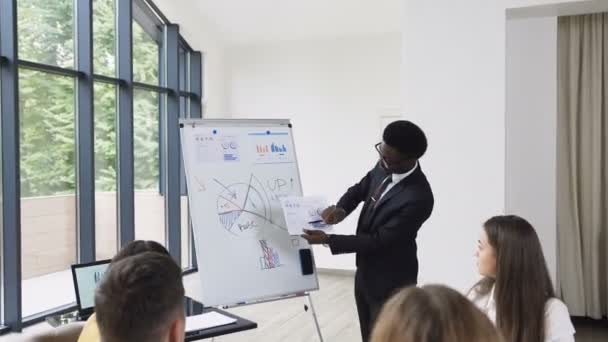 Homem americano-africano empresário realiza apresentação usando quadro branco em que mostra os gráficos de compra e venda da empresa, empresário dá apresentação, discutindo ideias com negócios diversos — Vídeo de Stock