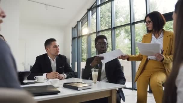 La joven líder del equipo caucásica da dirección al equipo de socios comerciales. Gente de negocios multiétnicos trabajan juntos en una reunión en una gran mesa de conferencias en una oficina moderna — Vídeos de Stock