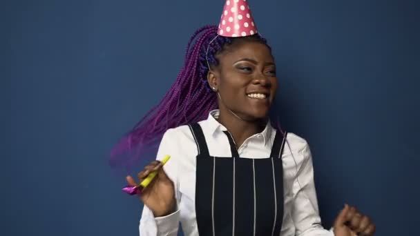 Handsome african girl in birthday hat dancing on the blue background. — Stock Video