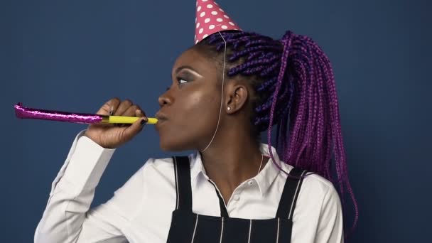 Sidovy av afrikanska ung kvinna i hatt Dans vissla i födelsedag horn på den blå bakgrunden. — Stockvideo