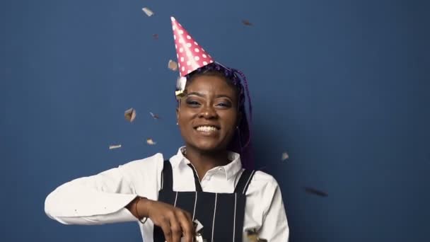 Knappe Afrikaanse vrouw dansen en gooien van gouden confetti op de blauwe achtergrond. — Stockvideo