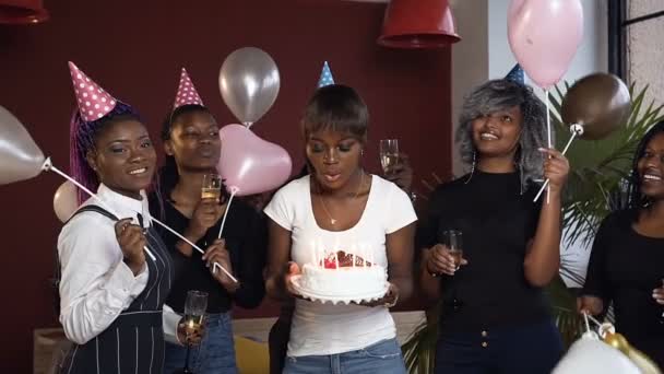 Feliz chica africana atractiva soplando velas en el pastel de cumpleaños rodeó a sus amigos . — Vídeo de stock