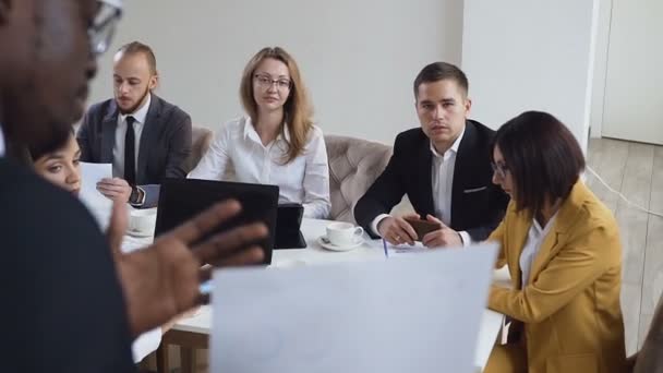 Une équipe concentrée de jeunes gens d'affaires multiethniques analyse des documents financiers montrant les revenus, les graphiques et le concept de travail d'équipe dans un bureau moderne. — Video