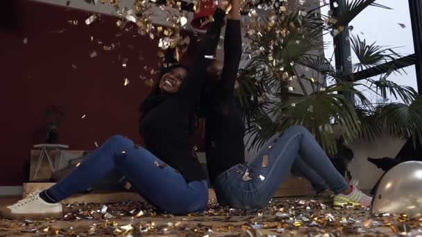 Mulheres africanas felizes jogando confetes de ouro enquanto sentadas no chão na sala vermelha . — Vídeo de Stock