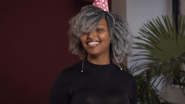 African girl in birthday hat with shampanage glass looking to the camera and dancing in the red room. — Stock Video