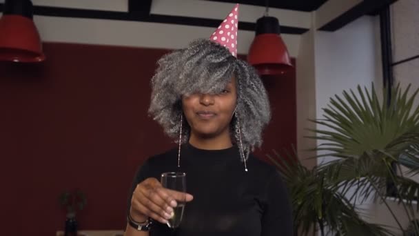 Portret van leuke Afrikaanse vrouw in hoed rammelende shampanage glas aan de camera in de rode kamer. — Stockvideo