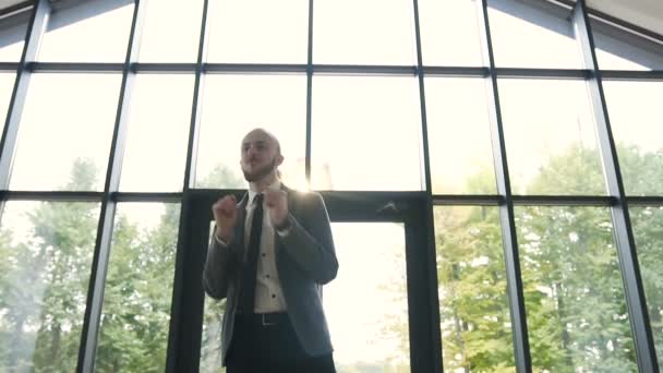 Счастливый молодой бизнесмен в костюме танцует в вестибюле офиса и празднует достижение на работе — стоковое видео