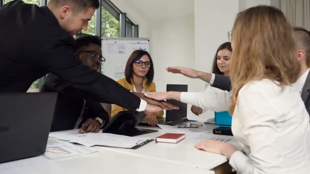 Joven grupo de personas de raza mixta pone las manos juntas en el centro de trabajo en la oficina moderna. Grupo de jóvenes empresarios que trabajan y se comunican sentados en el escritorio de la oficina — Vídeos de Stock