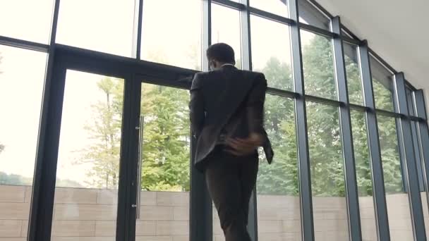 Happy young businessman dressed in suit is dancing in lobby of office with documents paper in hands, and celebrating achievement on work — Stock Video