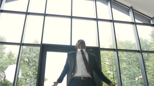 成功と幸せなアフロ アメリカ人実業家厳格なスーツを着てパノラマの窓の前にオフィスのホールで踊る彼の成果を祝います。仕事で後押し — ストック動画